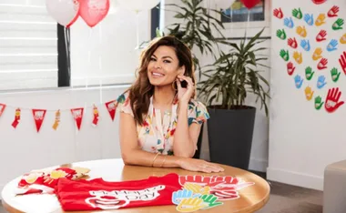 Smiling woman in a floral dress sits at a table with McHappy Day decorations and balloons in a festive room.