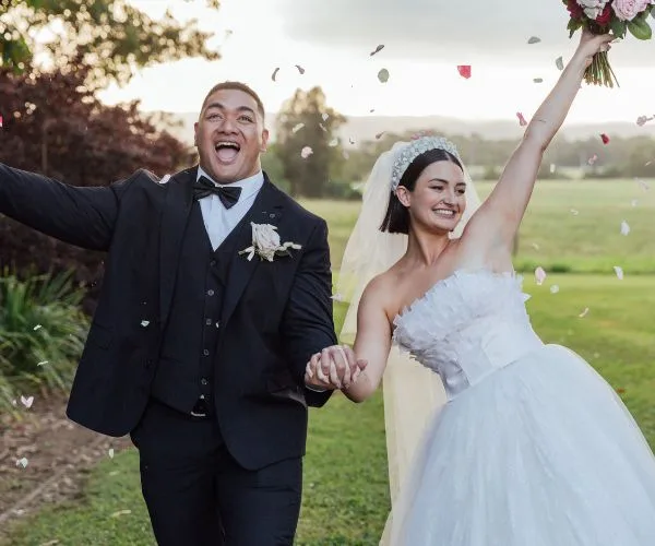 Wedding couple celebrating outdoors with confetti, bride in white holding bouquet, groom in black suit, smiling joyfully.