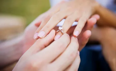 Hands placing a diamond ring on a finger, symbolizing engagement or proposal.
