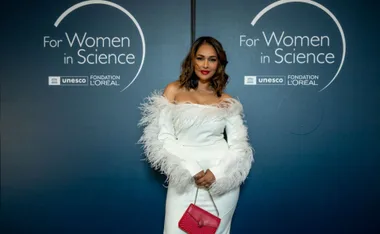 Woman in elegant white dress with red purse at "For Women in Science" event backdrop.