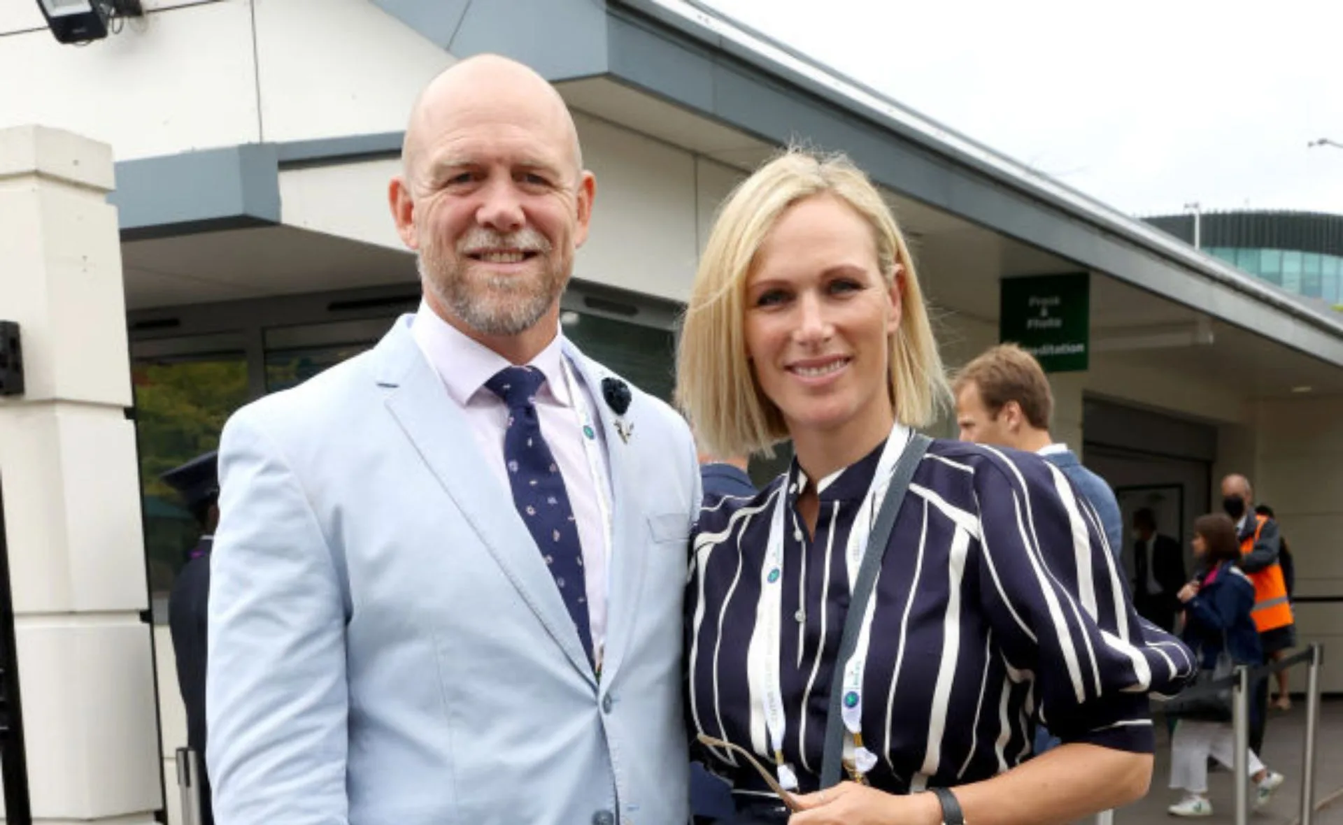 Man in a light blue suit with a woman in a striped dress smiling outdoors.