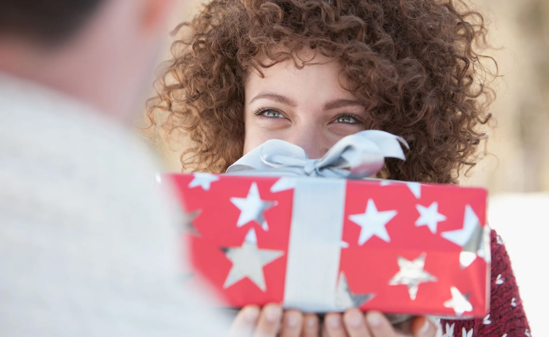 Person smiling, holding a red gift box with silver stars and a silver bow.