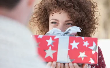 Person smiling, holding a red gift box with silver stars and a silver bow.