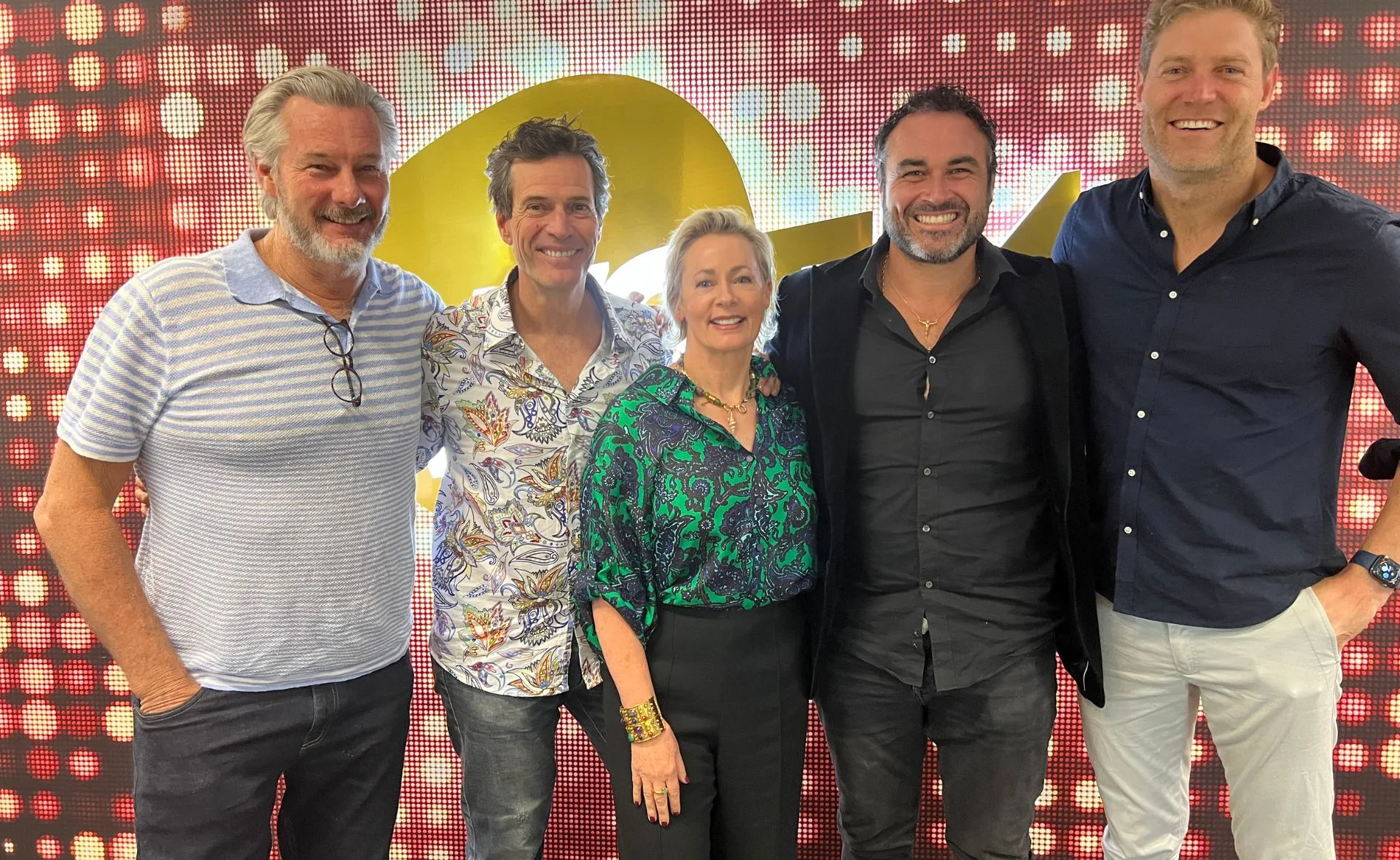 A group of five people standing together, smiling, in front of a colorful, illuminated backdrop.