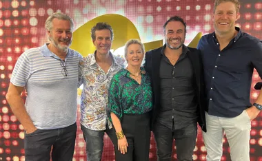 A group of five people standing together, smiling, in front of a colorful, illuminated backdrop.