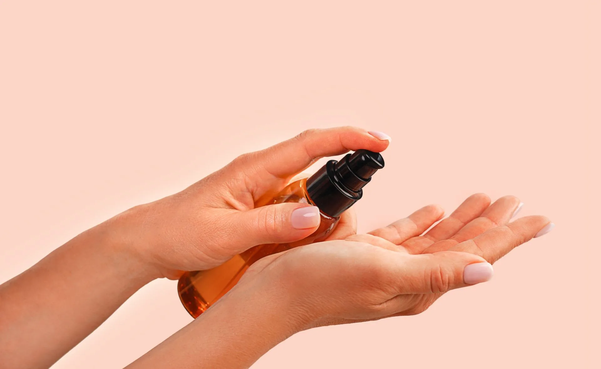 Hands applying a clear substance from a pump bottle onto one palm, over a peach-colored background.