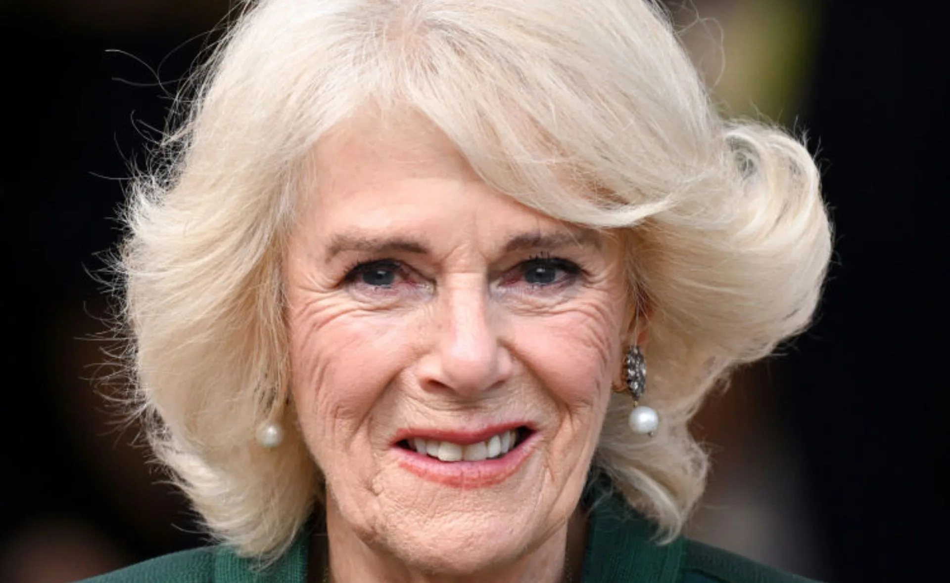 A woman with short blond hair and pearl earrings, smiling warmly at the camera.