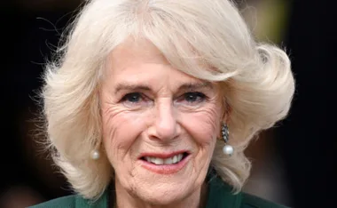 A woman with short blond hair and pearl earrings, smiling warmly at the camera.