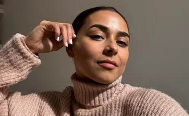 Person in a cozy pink sweater, taking a selfie with a relaxed expression and hand near face.