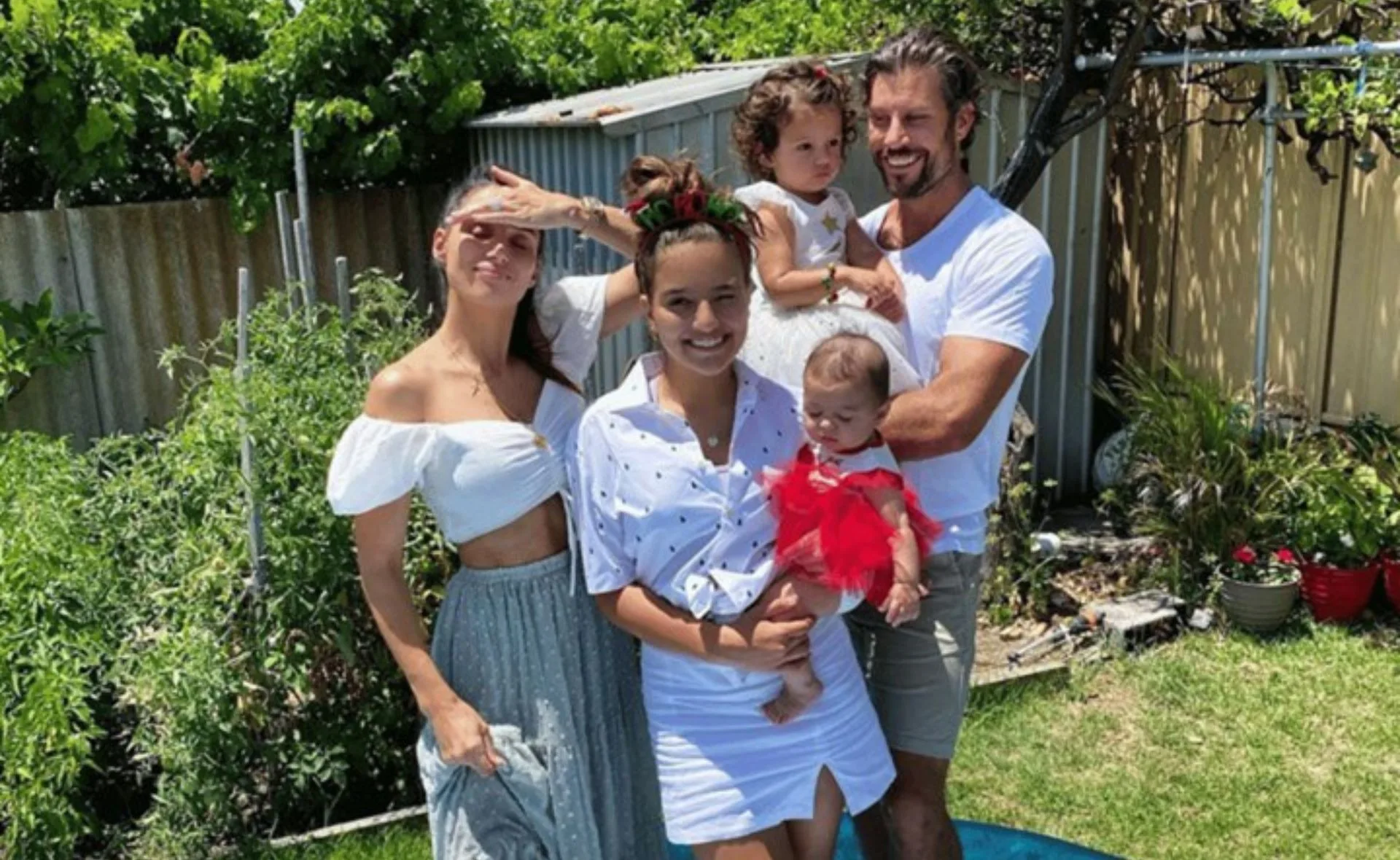 Family of five smiling in a garden, two adults and three children, two being carried.