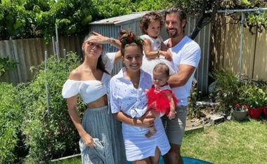Family of five smiling in a garden, two adults and three children, two being carried.