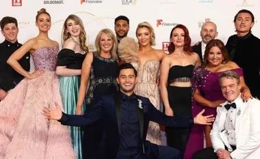 Group of people dressed in formal attire posing at a red carpet event.