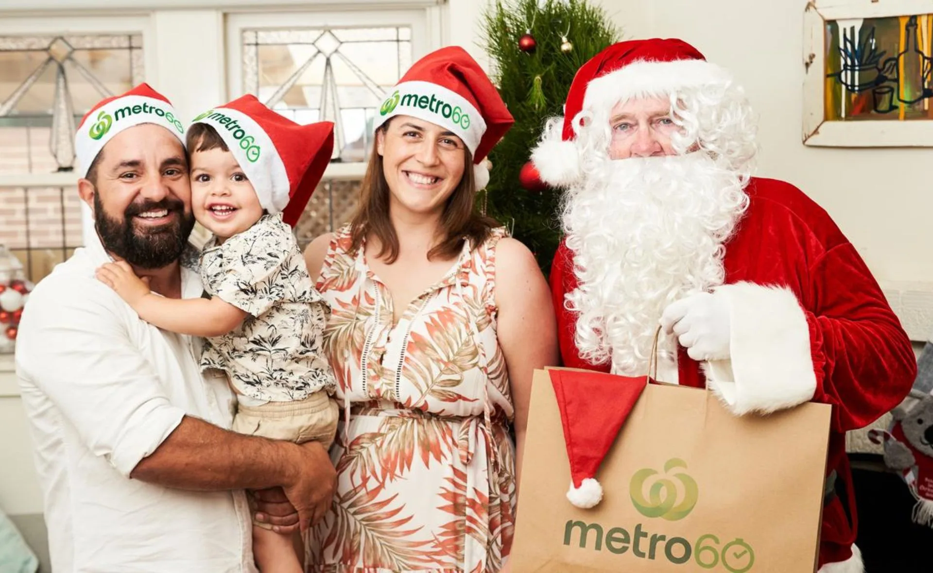 Family with Santa Claus in festive hats holding a shopping bag marked "metro60," standing in front of a Christmas tree.
