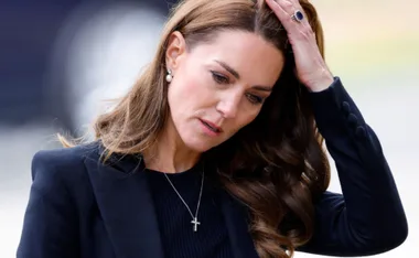 I don't know who this is, but it shows a woman in a black outfit touching her hair, wearing a pearl earring and cross necklace.