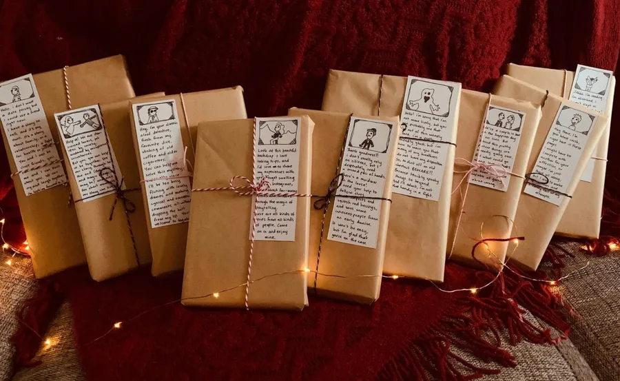 Brown-wrapped books with illustrated notes, twine ties, and fairy lights on a burgundy blanket.