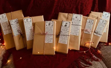 Brown-wrapped books with illustrated notes, twine ties, and fairy lights on a burgundy blanket.