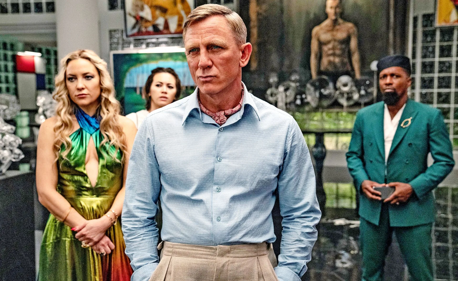 Four people stand in a sophisticated room; one man in a blue shirt appears focused.