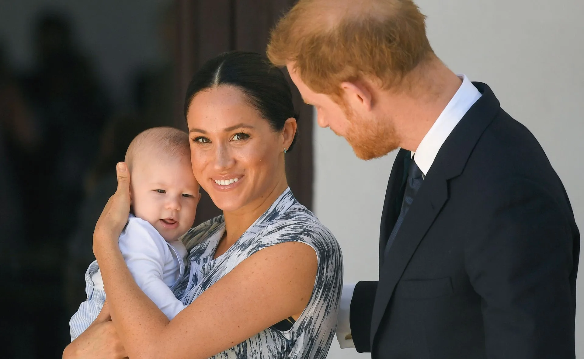 Prince Harry, Meghan Markle, and baby Archie smiling together outdoors.