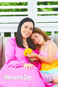 Woman in pink dress holding a sunflower sits with a young girl in a colorful dress.