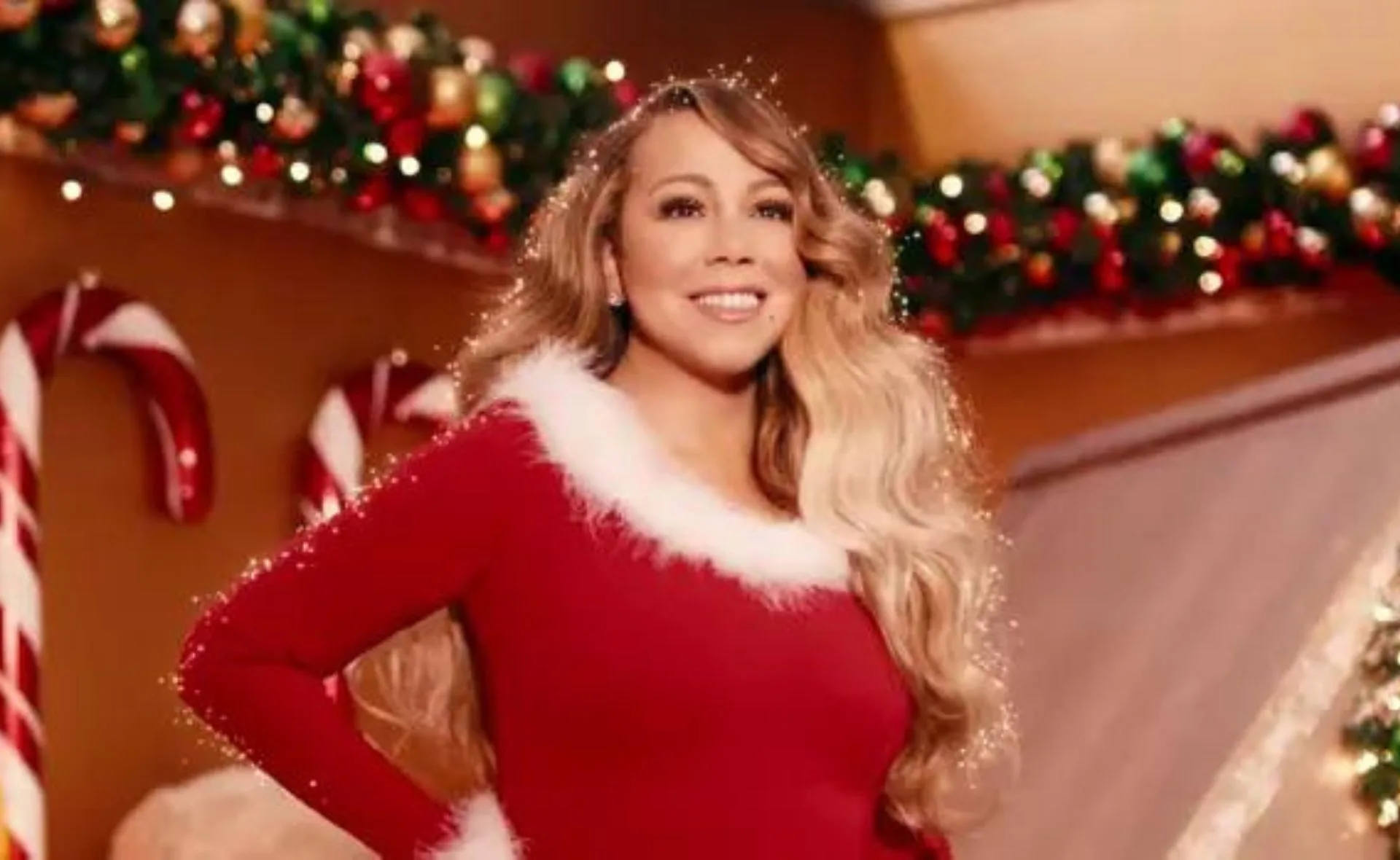A woman in a red and white outfit stands in a festive room with candy canes and holiday decorations in the background.