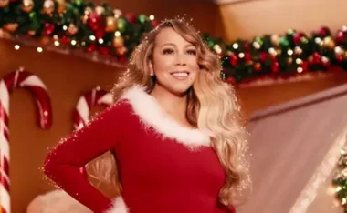 A woman in a red and white outfit stands in a festive room with candy canes and holiday decorations in the background.