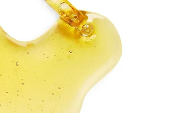 Close-up of a golden sandalwood oil spill with bubbles on a white background.