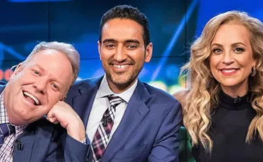 Three smiling hosts in formal attire posing together.
