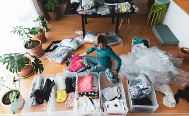 Woman organizing clothes into boxes in a room with plants.