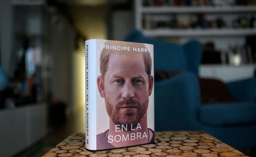 Cover of "Príncipe Harry: En La Sombra" book, focused on Prince Harry's face, on a wooden table indoors.