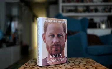 Cover of "Príncipe Harry: En La Sombra" book, focused on Prince Harry's face, on a wooden table indoors.