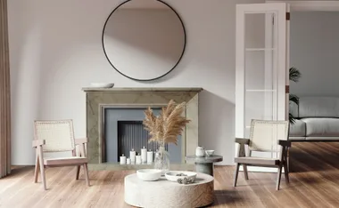 Modern living room with fireplace, round mirror, two chairs, and a coffee table with decor and pampas grass.