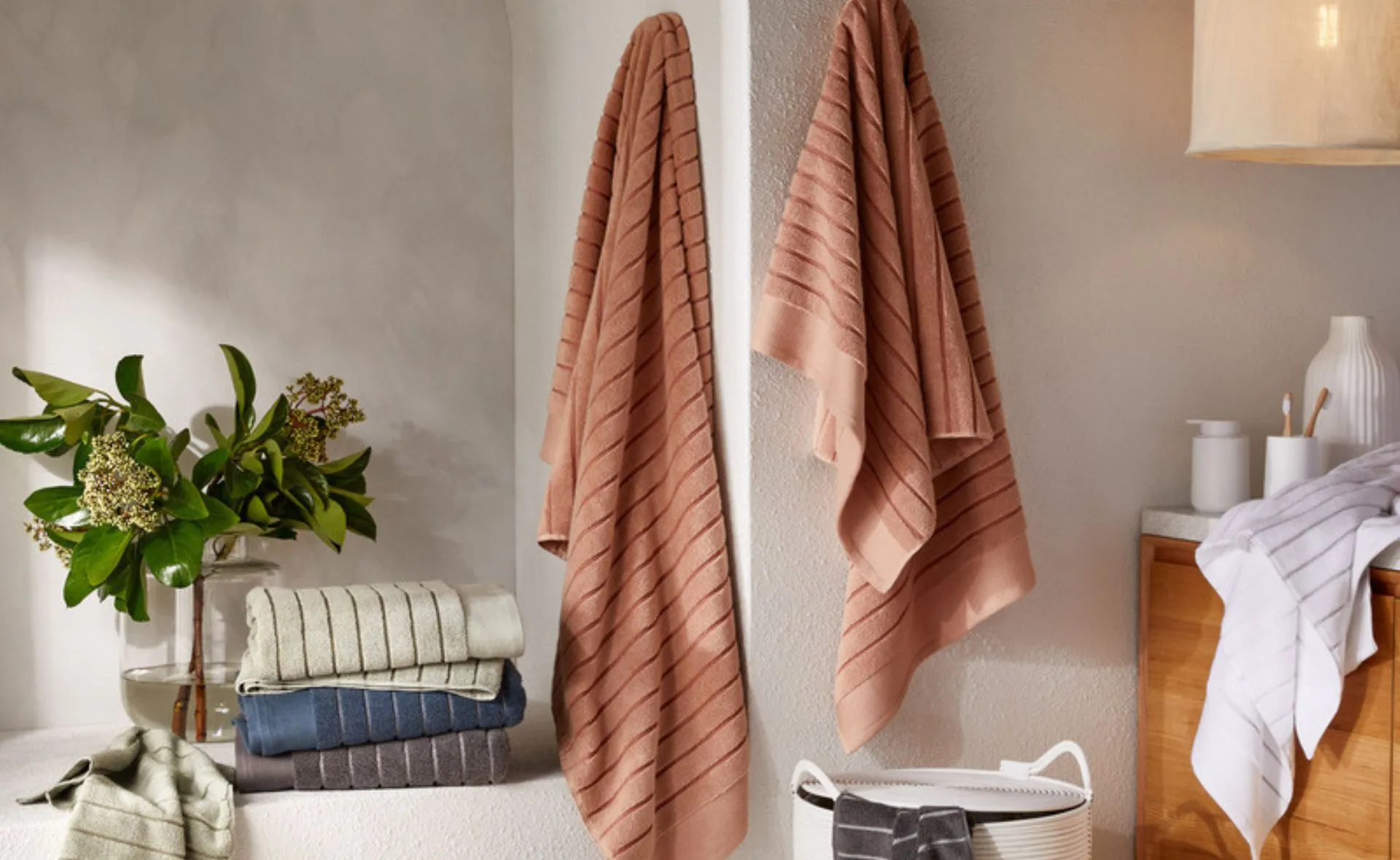 Cozy bathroom setting with folded and hanging striped towels, plants, and a basket.
