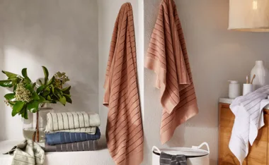 Cozy bathroom setting with folded and hanging striped towels, plants, and a basket.
