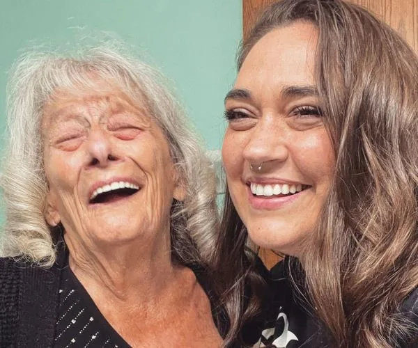 Two women smiling warmly; an elderly woman with gray hair and a younger woman with long brown hair share a joyful moment.