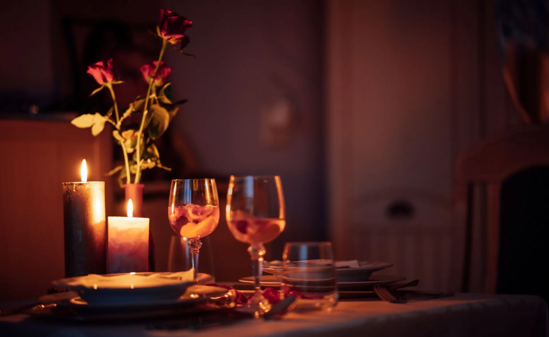 Candle-lit dinner table with roses, wine glasses, and plates set for two, creating a romantic ambiance.