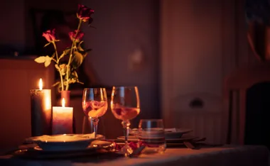 Candle-lit dinner table with roses, wine glasses, and plates set for two, creating a romantic ambiance.