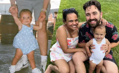 A baby held up by an adult alongside a smiling family with a woman, man, and toddler in sunny outdoor setting.