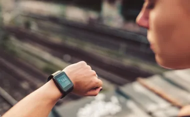 A person checking a smartwatch displaying a heart rate of 144 bpm, with blurred train tracks in the background.