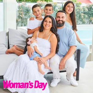A family of six, including a couple and four children, smiling and sitting on a modern outdoor sofa by a pool, featured in Woman's Day.