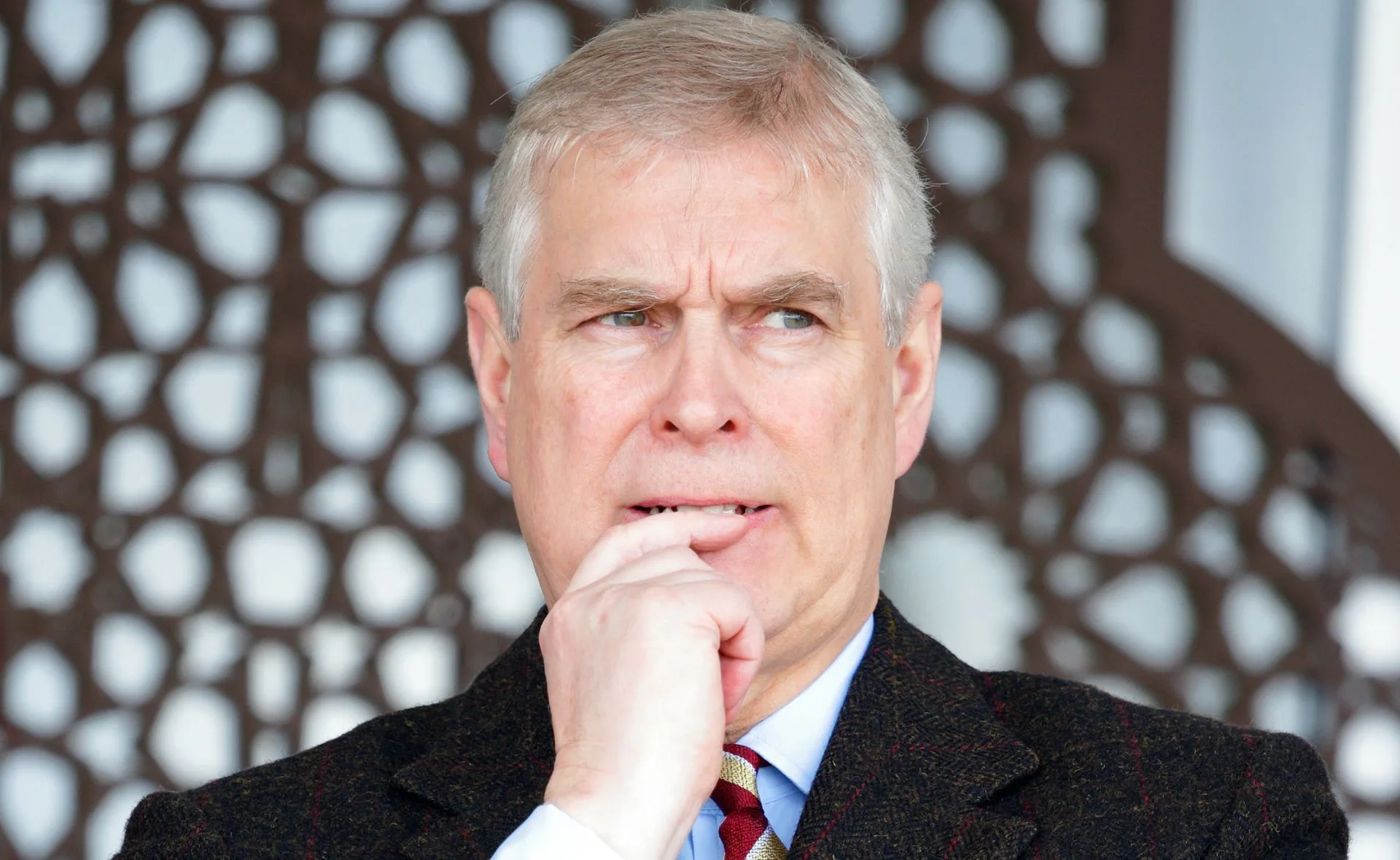 A man looking thoughtful, wearing a suit with a patterned background.