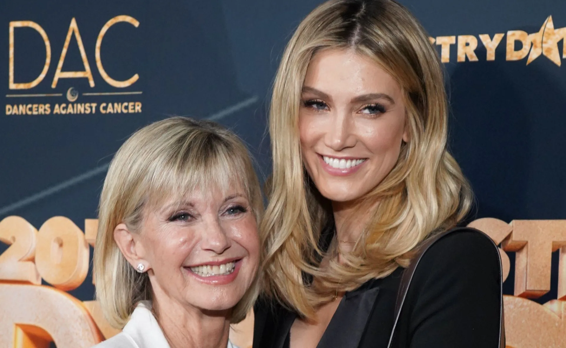 Two women smiling at a Dancers Against Cancer event, standing closely together.