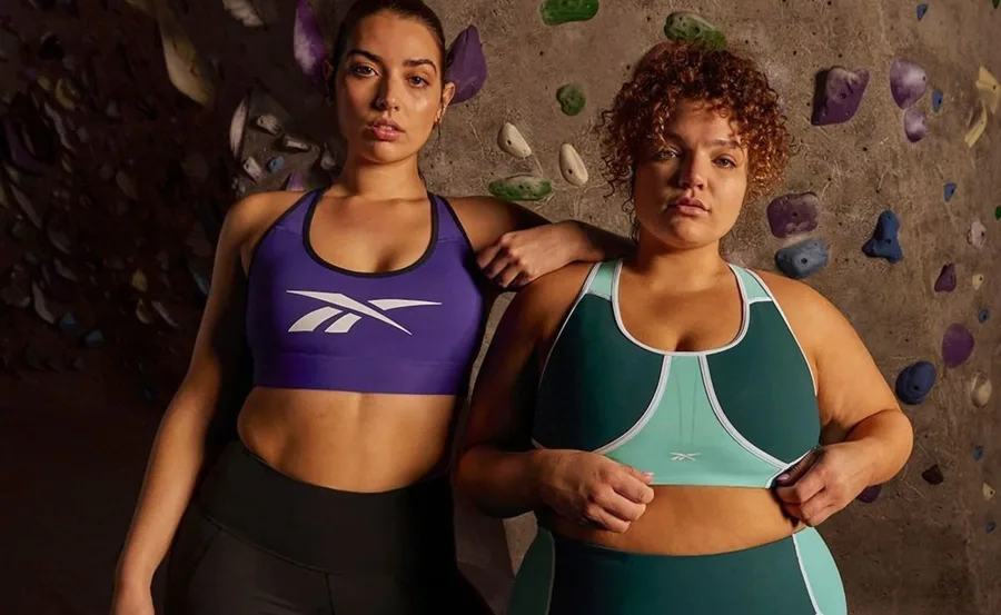Two women in Reebok activewear posing in front of a climbing wall.