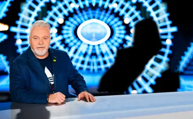 Man with white beard in blue suit in front of abstract blue circular pattern on a TV set.