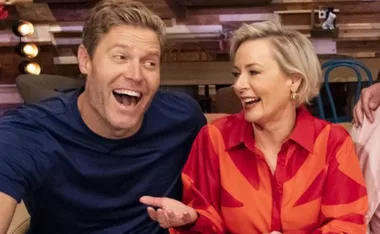 Laughing man and woman seated together in a casual setting, enjoying a light-hearted moment.