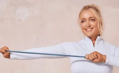 Woman exercising with a resistance band, smiling, wearing a light blue top.