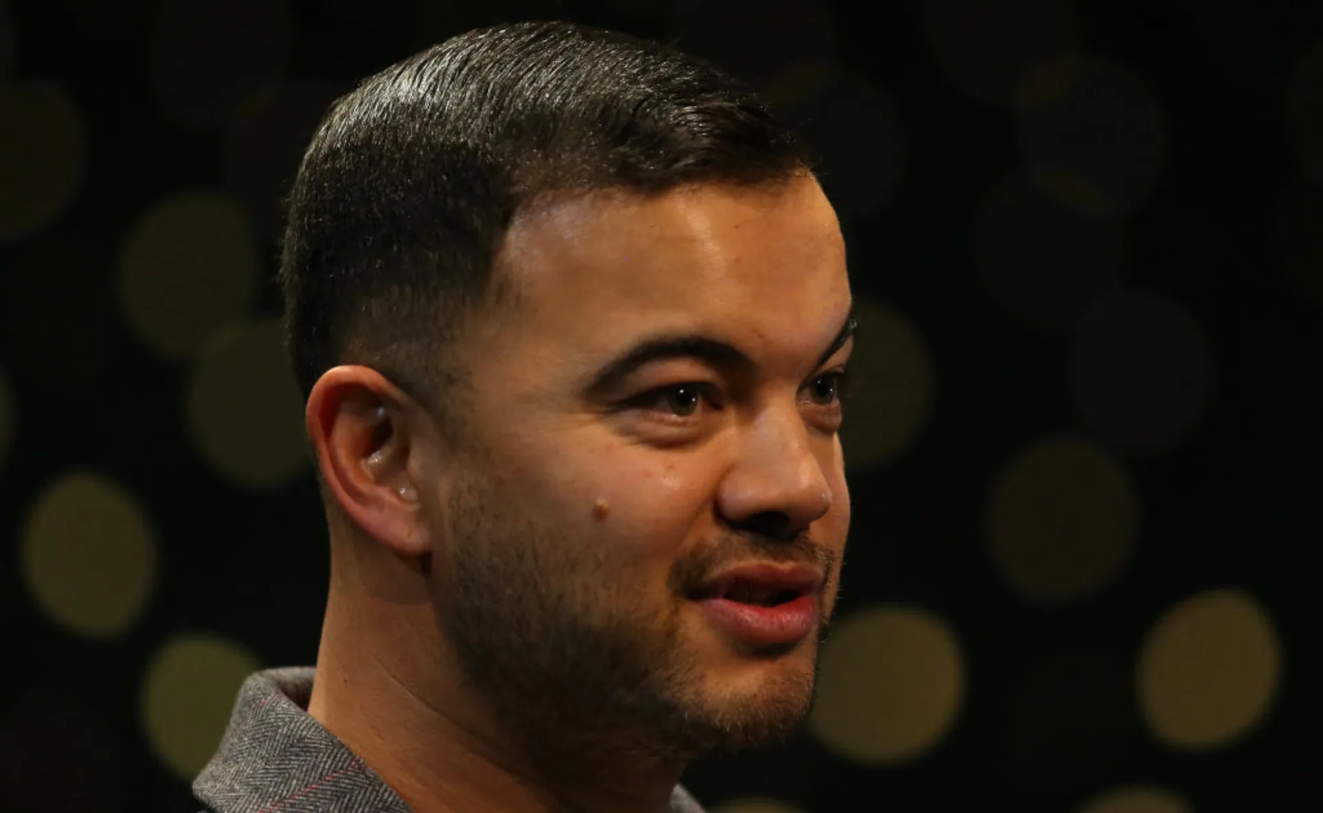 A person with short dark hair and a trimmed beard, facing slightly right against a dark blurred background.