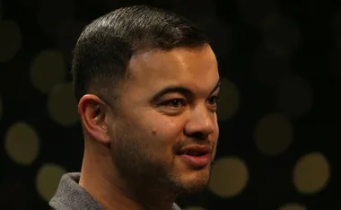 A person with short dark hair and a trimmed beard, facing slightly right against a dark blurred background.