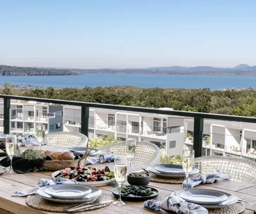 Alfresco dining setup with plates and champagne overlooking coastal view and modern villas in Noosa, Australia.