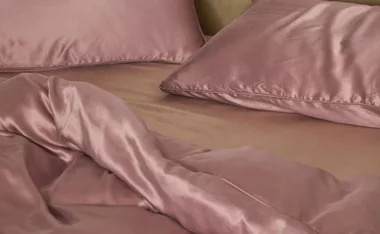 Luxurious pink silk bed sheets and pillowcases on a bed.