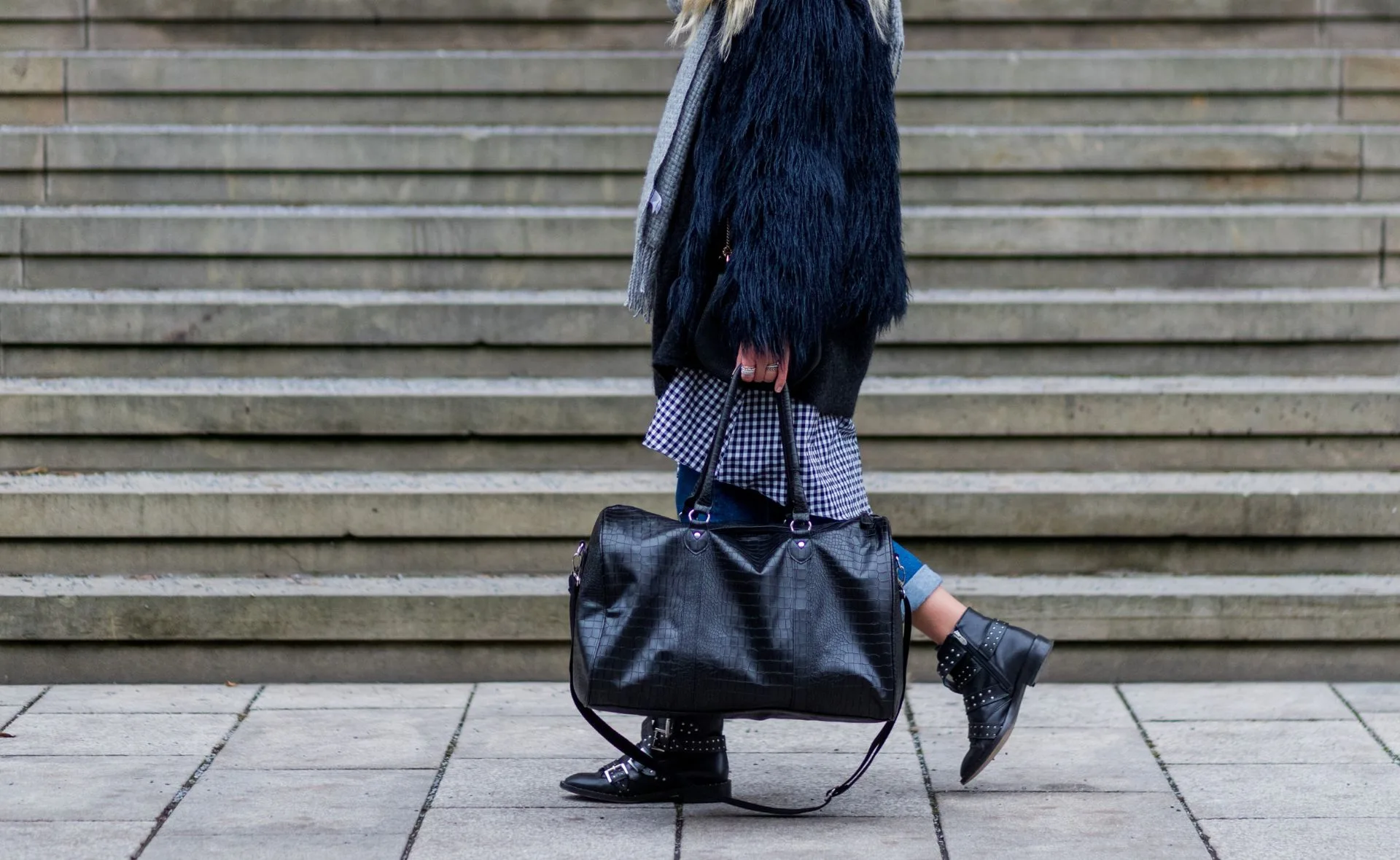 Person walking with a black leather weekender bag on stone steps.